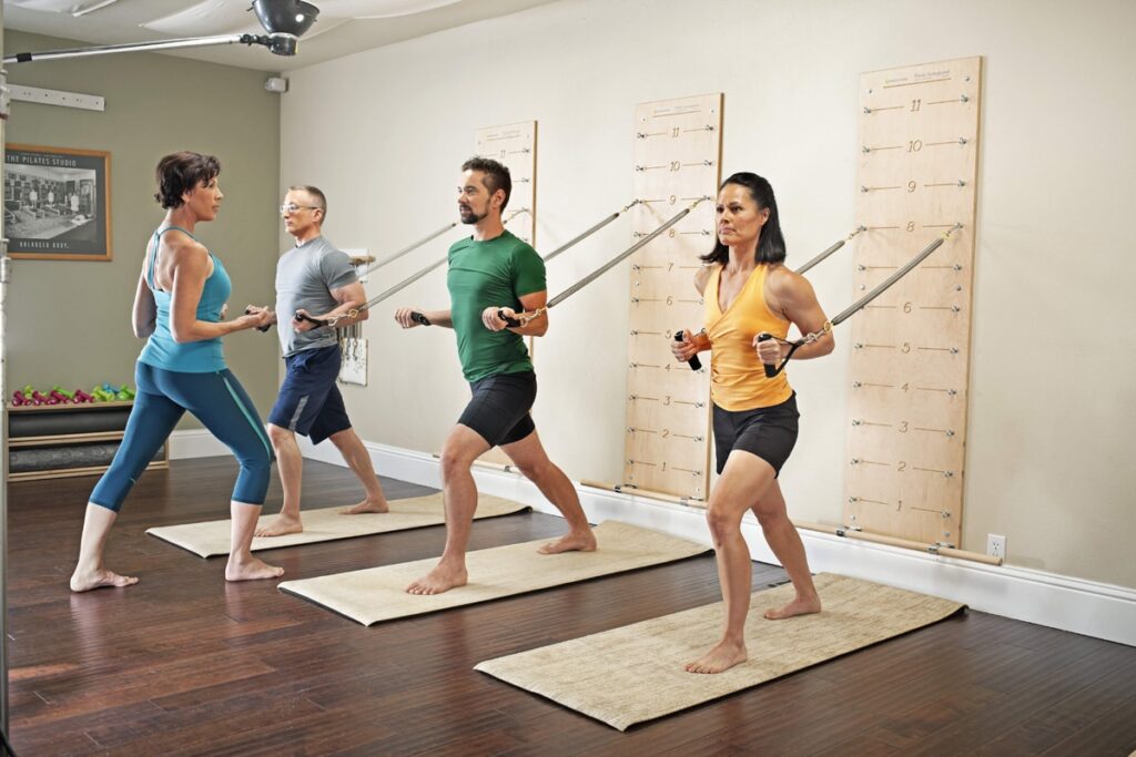 Four people exercising with Pilates Springboards mounted on a wall.