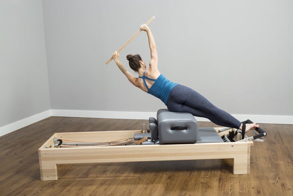 Person exercising on CenterLine Reformer with wooden pole.