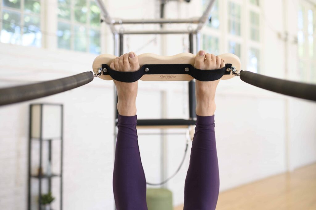 User performing exercise on Contrology Cadillac trapeze bar