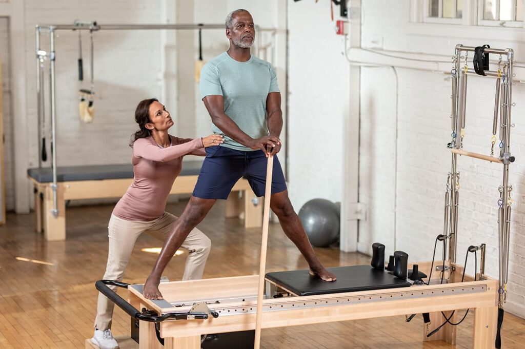 Instructor assisting a client on Clinical Reformer with Tower.