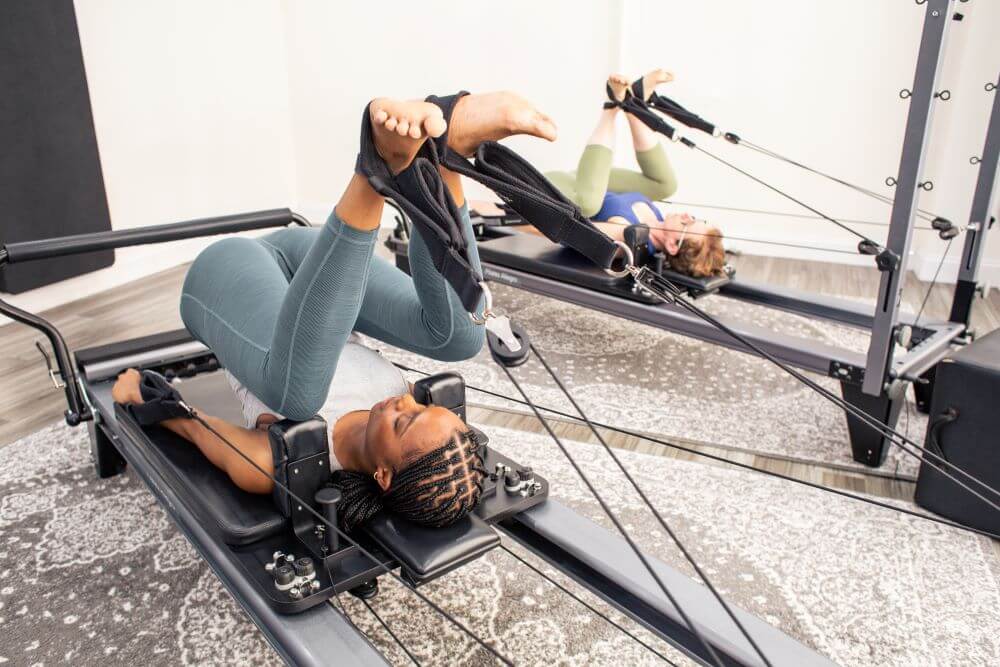 Two individuals using Allegro Reformer Konnector in Pilates studio.
