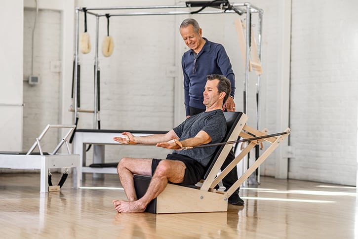 Man exercising on Contrology Arm Chair in Pilates studio.
