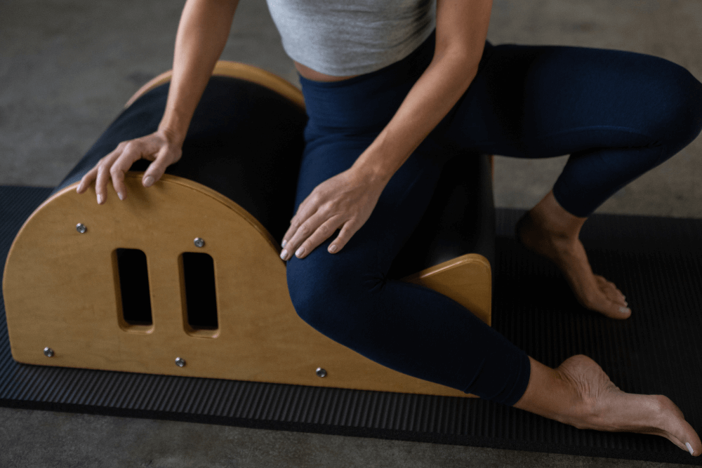 Person using Clara Step Barrel for Pilates exercise on mat.