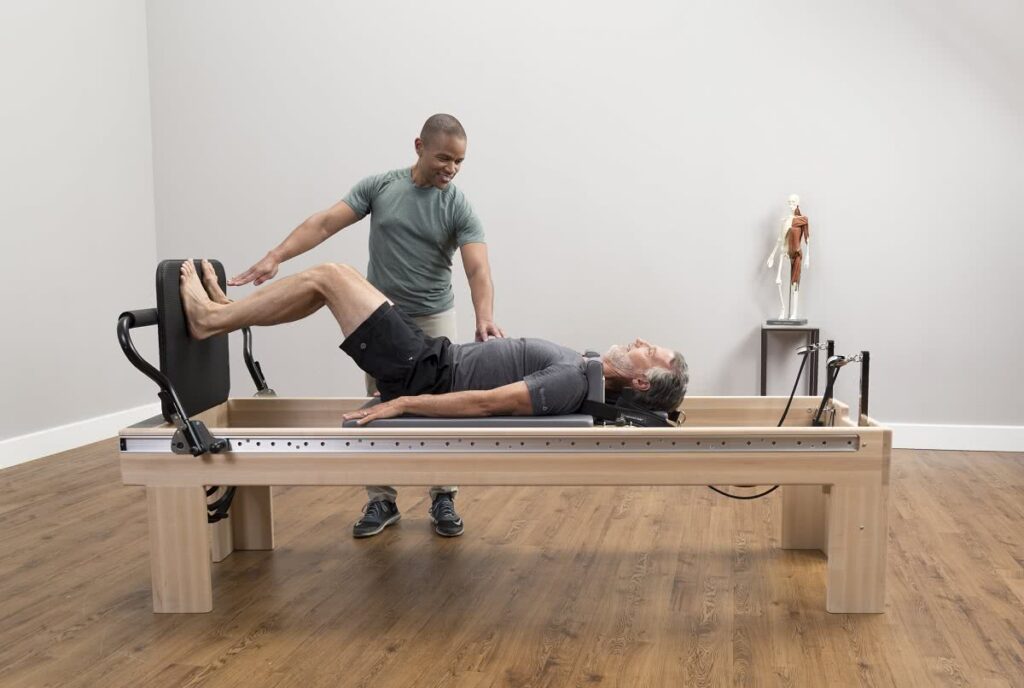 Instructor assisting man on Clinical Reformer Pilates machine.