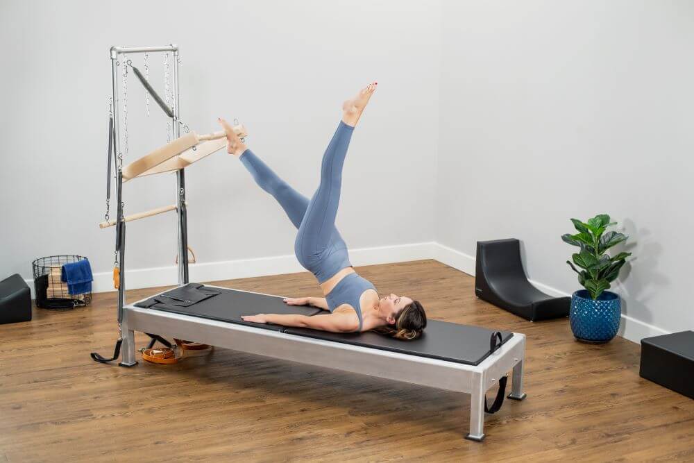 Woman exercising on Contrology Reformer with Tower and Mat.