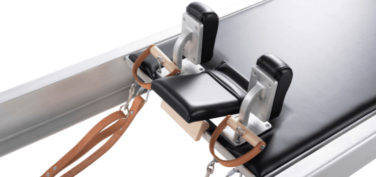 Pilates carriage with black upholstery and wooden headrest lock.
