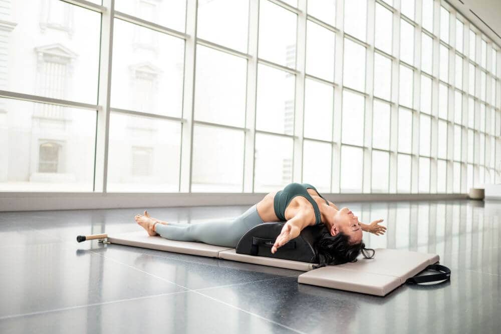 Woman stretching on Contrology Small Barrel in bright studio.
