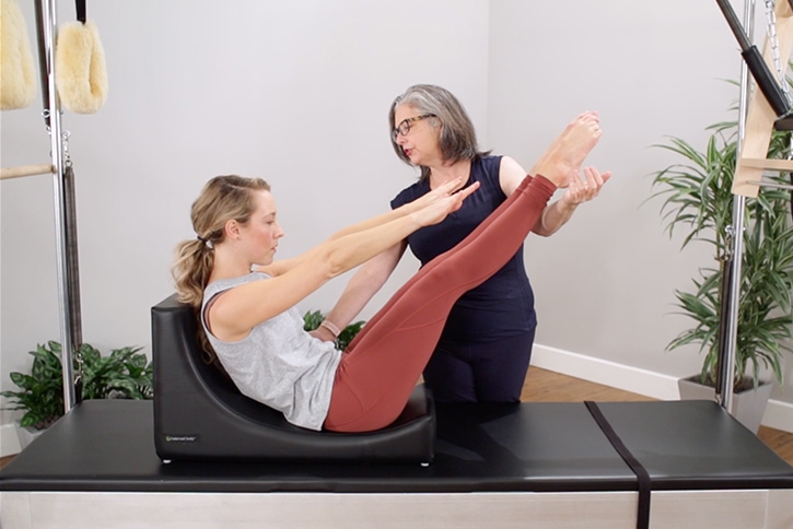 Instructor assisting Pilates exercise on C-Shaper equipment.