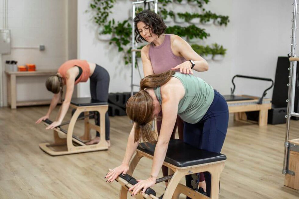 Instructor assisting student on EXO Chair during Pilates class.