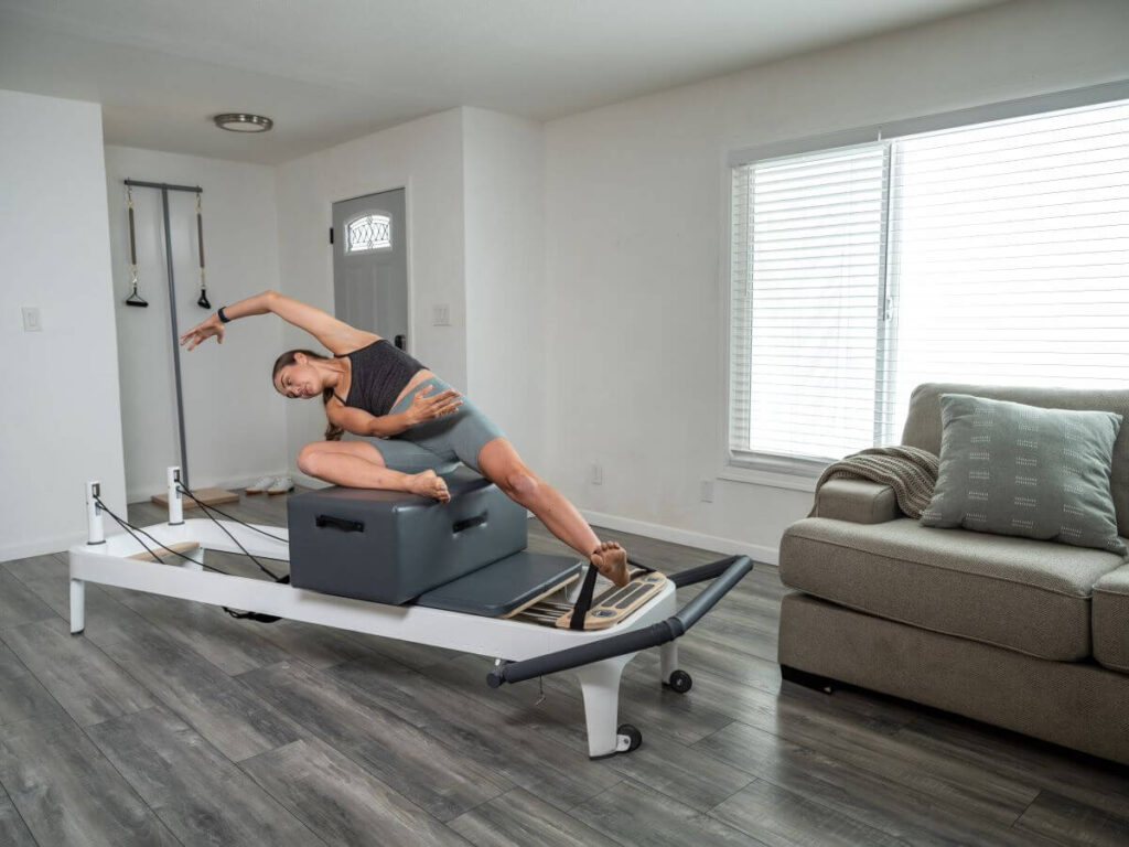 Woman uses Footstraps in Pilates Mermaid pose on reformer with Sitting Box