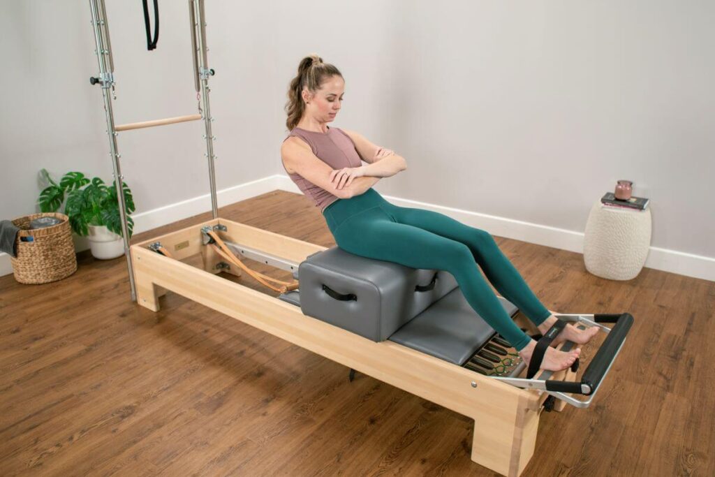 Pilates reformer with Sitting Box and Footstraps in use.
