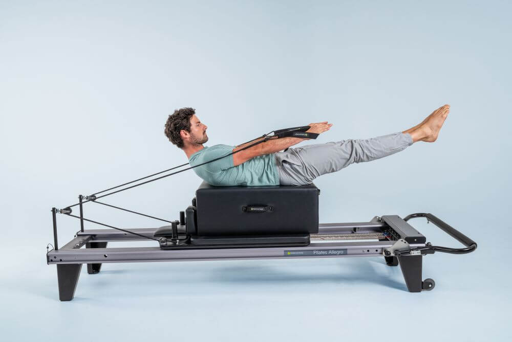 Man exercising on Allegro Reformer Pilates equipment in a studio.