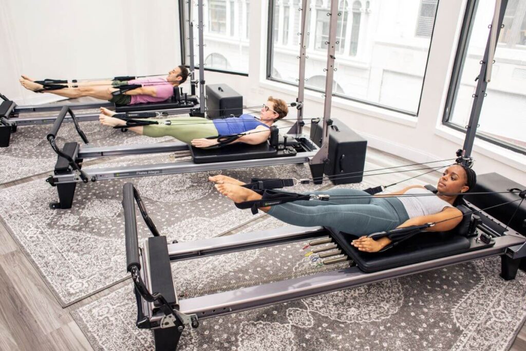 Three people using Pilates reformers with Signature Springs.