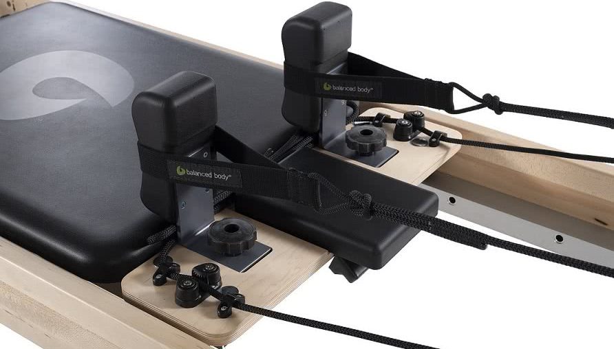 Pilates reformer carriage with adjustable shoulder rests and black upholstery.
