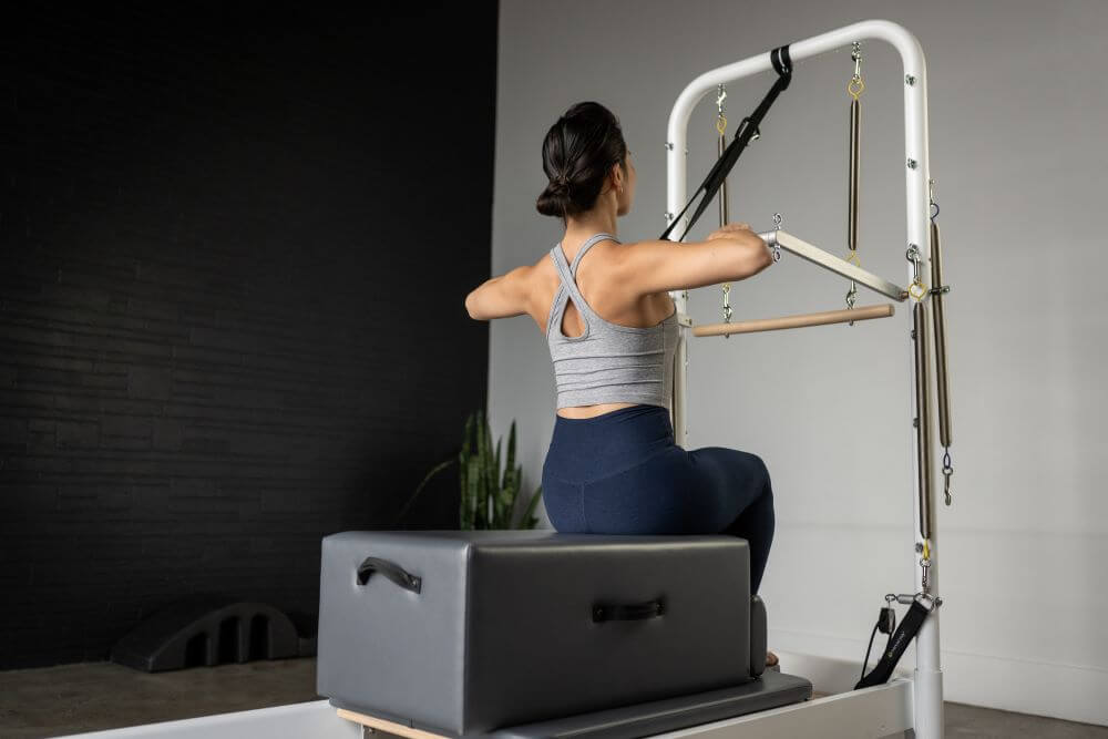 Woman using Standard Sitting Box on Pilates reformer for exercise.