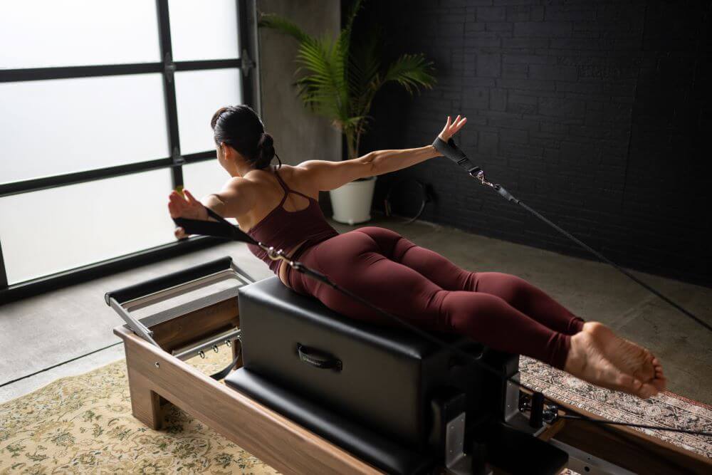 Person performing Pilates on a reformer with Standard Sitting Box.