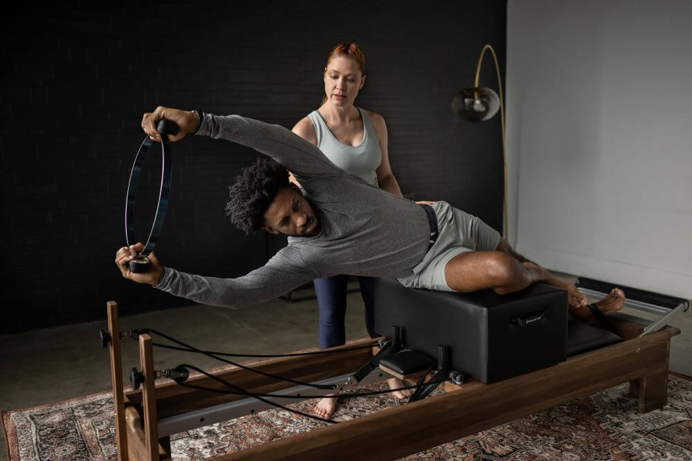 Pilates instructor assisting a client on Standard Sitting Box with reformer.