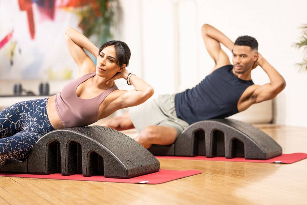 Two people exercising on Pilates Arcs in a studio setting.