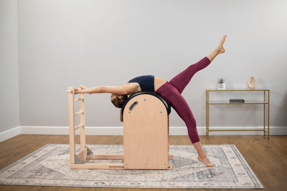 Woman stretching on a Balanced Body Ladder Barrel for Pilates.
