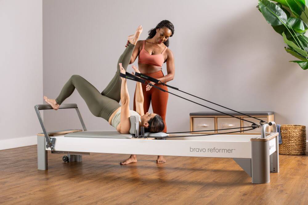 Instructor assisting client on Bravo Reformer Pilates machine.