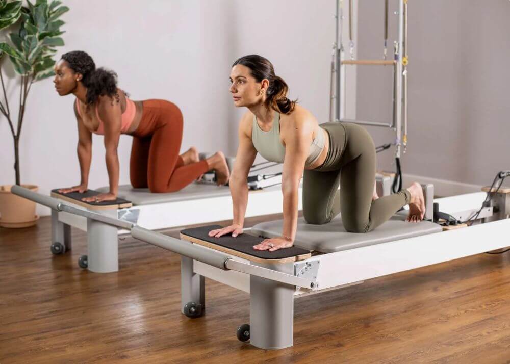 Two women practicing on Bravo Reformer Platform Extenders.